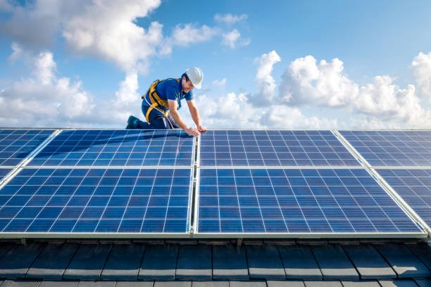 Male engineer in blue suit and protective helmet installing photovoltaic panel system. Professional electrician mounting solar module on roof. Alternative energy ecological concept